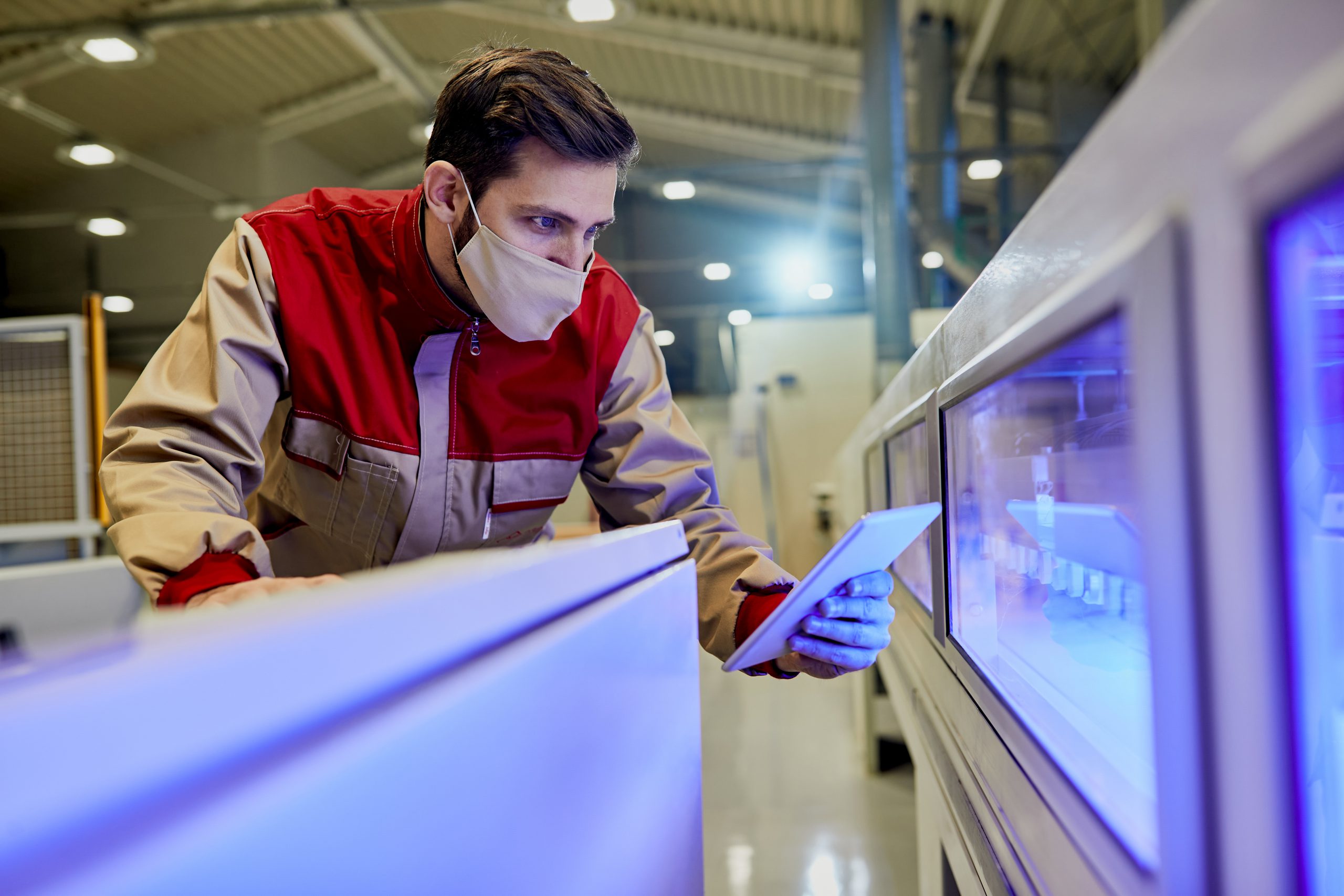 Operator w masce ochronnej nadzorujący pracę linii obróbczej przy pomocy panelu połączonego z systemem kontroli produkcji kraków.